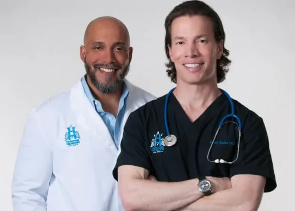 Dr. Jason Burke, in black scrubs embroidered with his name, beside a colleague in a white Hangover Heaven coat