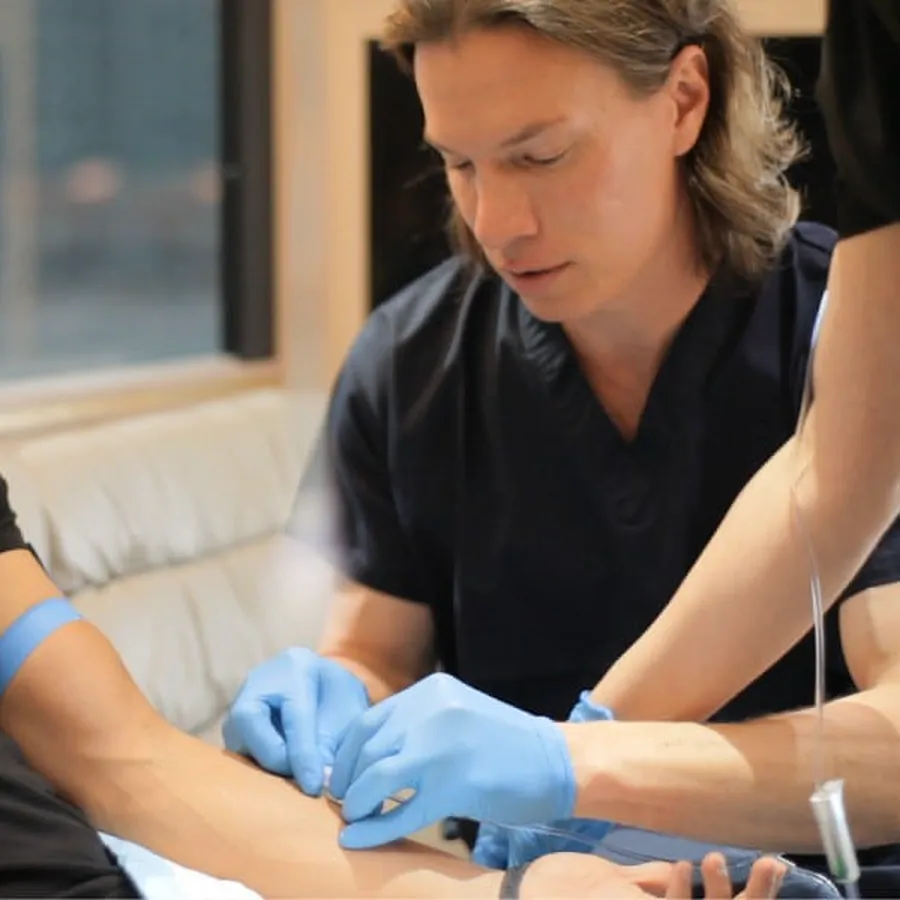 A Hangover Heaven clinician in navy scrubs and blue gloves places an IV in a patient's arm