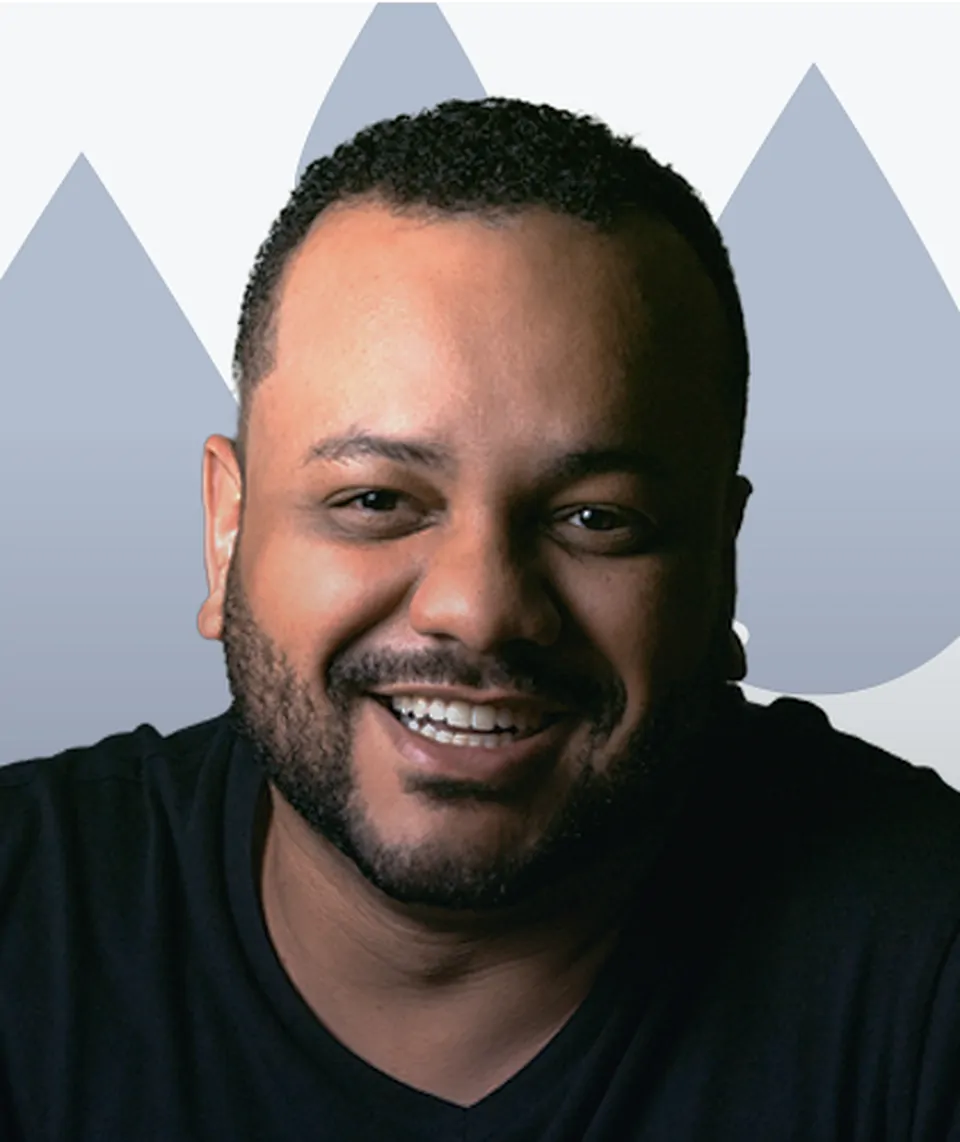 A bearded man in a black T-shirt laughs toward the camera, in front of the brand's blue droplet shapes